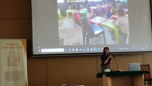 na zdjęciu Pani Martyna Zaremba, która opowiada o swojej posłudze misyjnej, w tle wyświetlone zdjęcie prezentujące placówkę misyjną - szkołę.